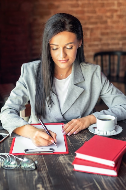 Young woman is writing plans in notebook at the table in modern interior cafe.