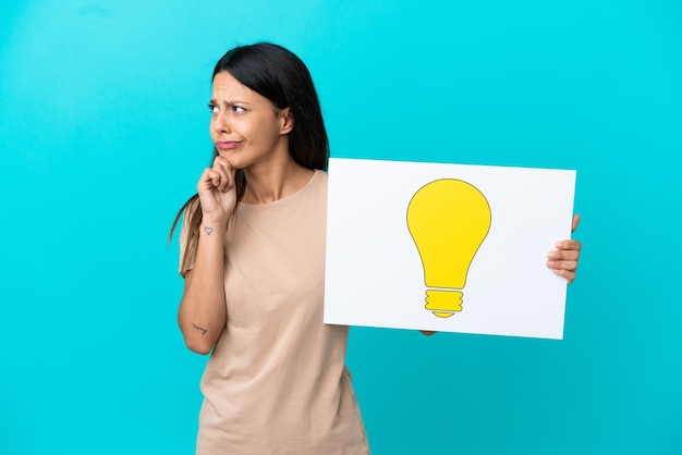 Young woman over isolated background holding a placard with bulb icon and thinking