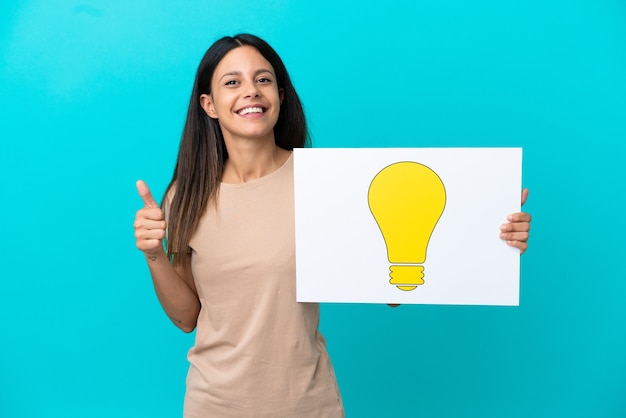 Young woman over isolated background holding a placard with bulb icon with thumb up