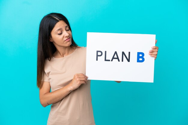 Photo young woman over isolated background holding a placard with the message plan b with sad expression