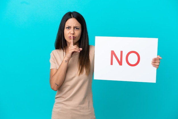 Young woman over isolated background holding a placard with text NO doing silence gesture