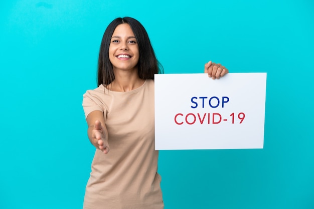 Young woman over isolated background holding a placard with text Stop Covid 19 making a deal