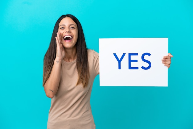 Young woman over isolated background holding a placard with text YES and shouting