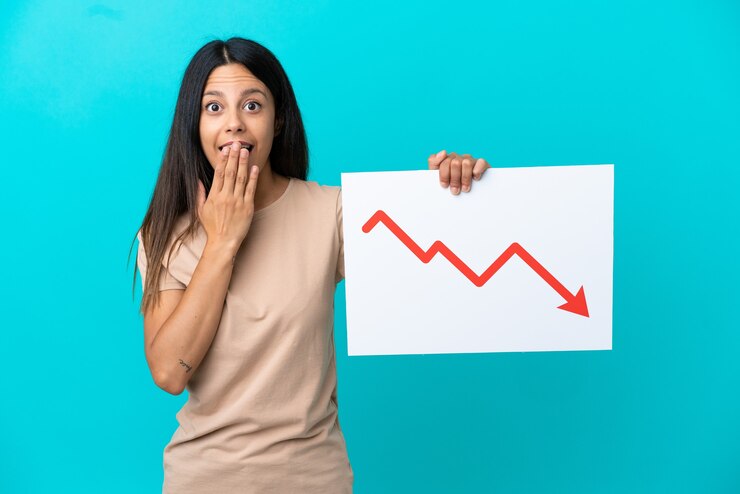 फोटो young woman over isolated background holding a sign with a decreasing statistics arrow symbol with surprised expression