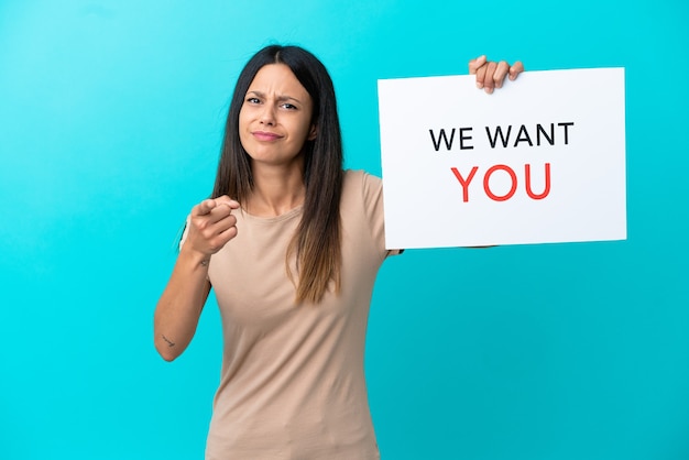 Young woman over isolated background holding We Want You board and pointing to the front