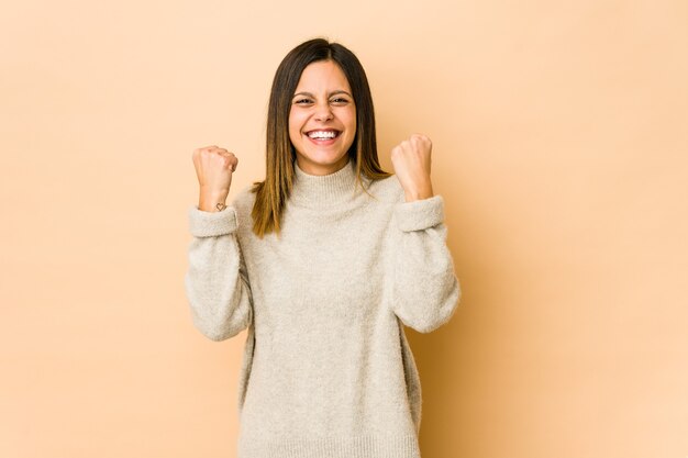 Young woman isolated on beige cheering carefree and excited.