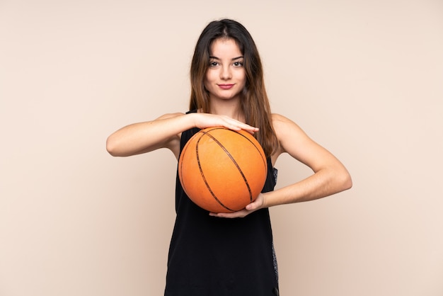 Young woman isolated on beige playing basketball