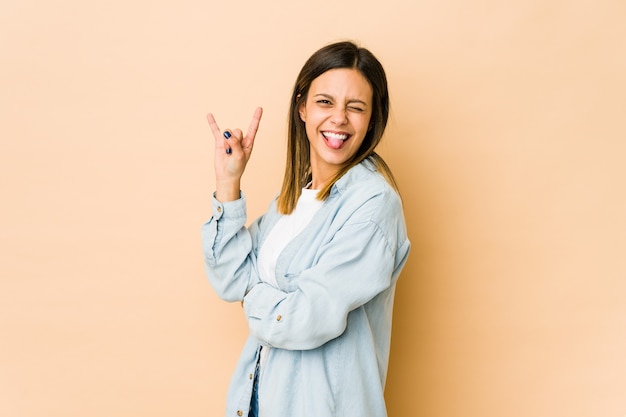 Young woman isolated on beige showing rock gesture with fingers