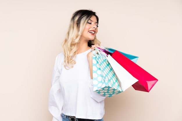 Young woman isolated on beige wall holding shopping bags and smiling