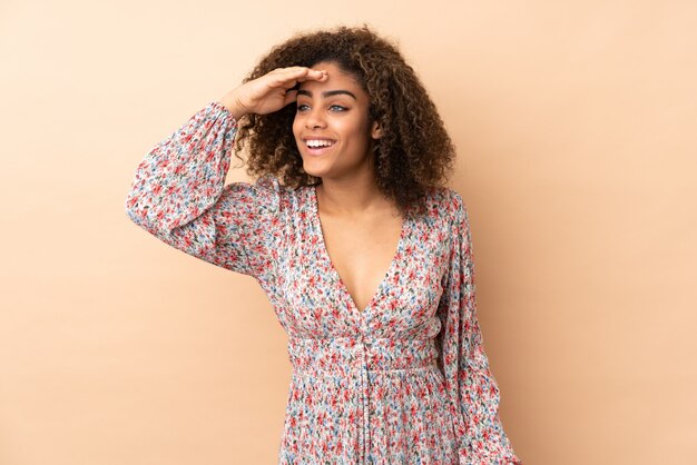 Young woman isolated on beige wall looking far away with hand to look something