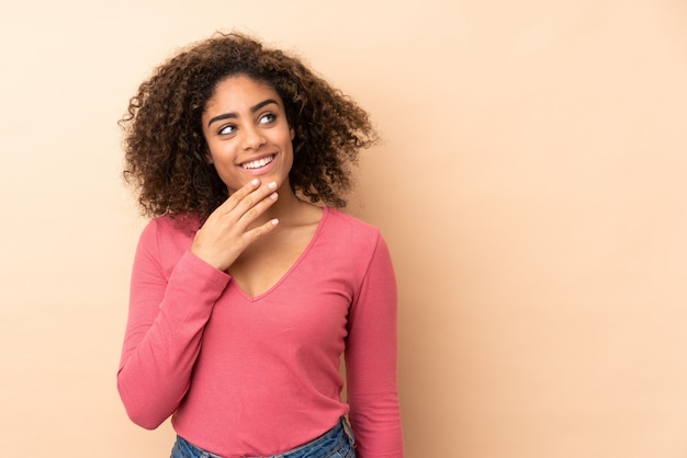 Young woman isolated on beige wall looking up while smiling