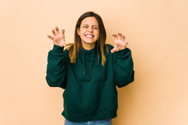 Young woman isolated on beige wall showing claws imitating a cat, aggressive gesture.