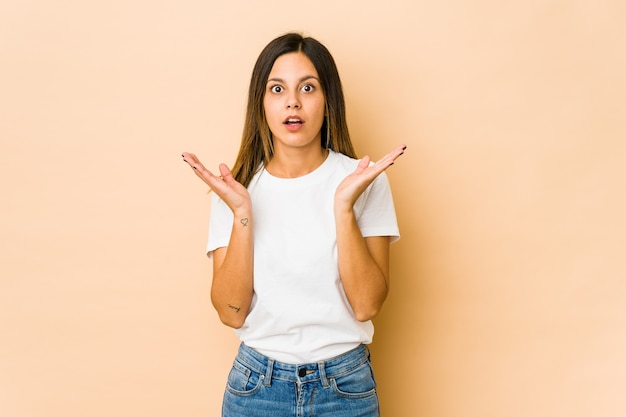 Young woman isolated on beige wall surprised and shocked