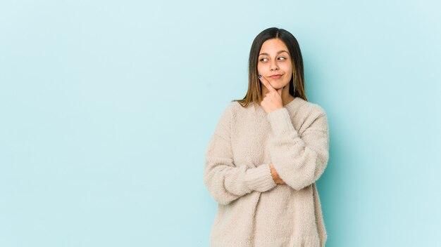 Young woman isolated on blue background contemplating, planning a strategy, thinking about the way of a business.