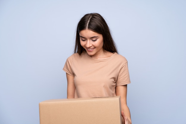 Young woman over isolated blue background holding a box to move it to another site