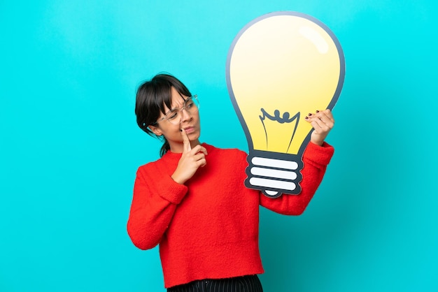 Foto giovane donna isolata su sfondo blu che tiene un'icona della lampadina e che ha dei dubbi