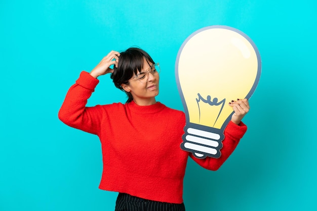 Young woman isolated on blue background holding a bulb icon and having doubts