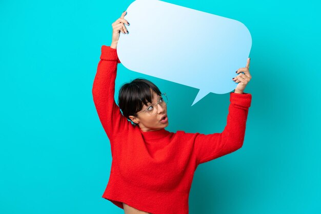 Young woman isolated on blue background holding an empty speech bubble and with sad expression