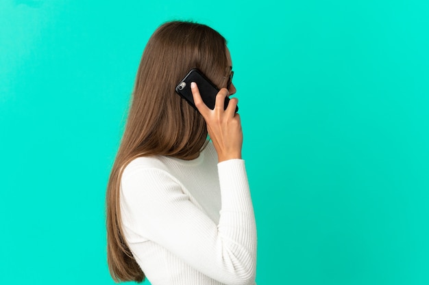 Молодая женщина на изолированном синем фоне разговаривает по мобильному телефону с кем-то