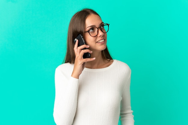 Молодая женщина на изолированном синем фоне разговаривает по мобильному телефону с кем-то