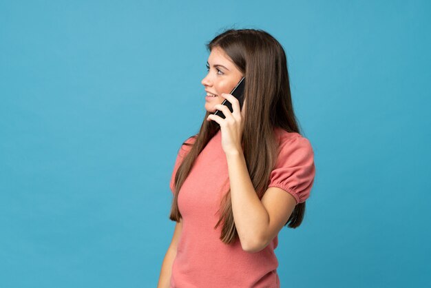 Foto giovane donna su sfondo blu isolato mantenendo una conversazione con il telefono cellulare con qualcuno