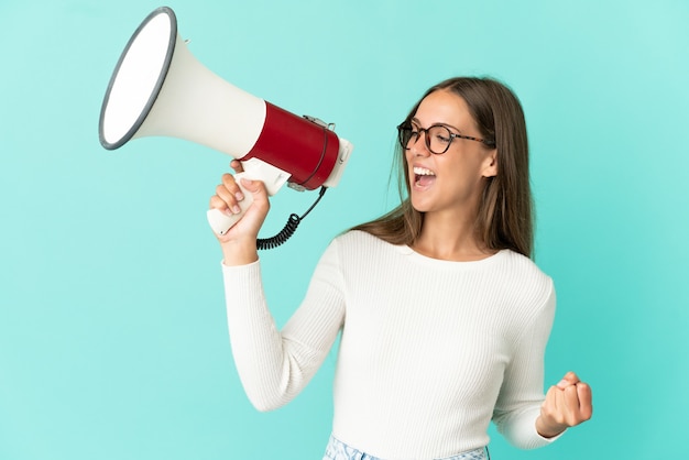 Young woman over isolated blue background shouting through a megaphone to announce something in lateral position