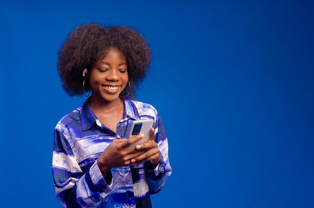 Young woman isolated on blue background smiling using her mobile