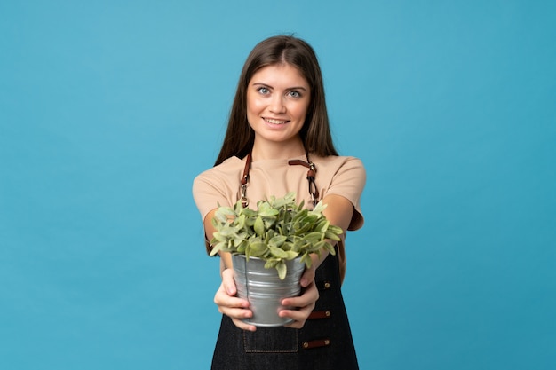 Young woman over isolated blue background taking a flowerpot