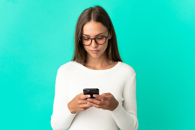 Young woman over isolated blue background using mobile phone