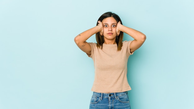 Young woman isolated on blue covering ears with hands trying not to hear too loud sound.