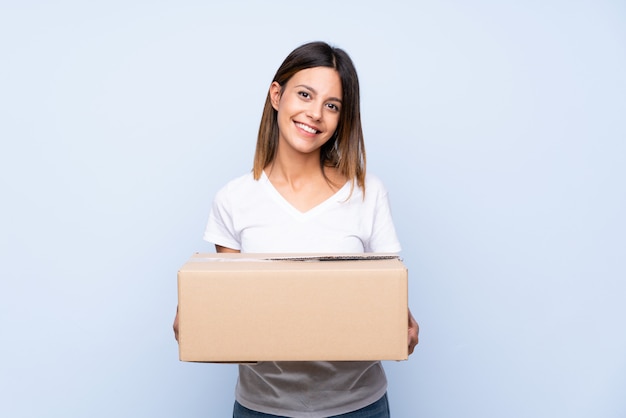 Young woman over isolated blue holding a box to move it to another site