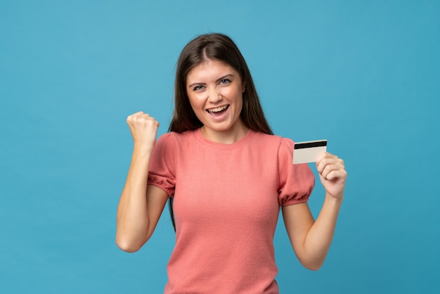 Young woman over isolated blue holding a credit card