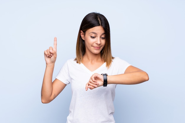 Young woman over isolated blue looking at the hand watch