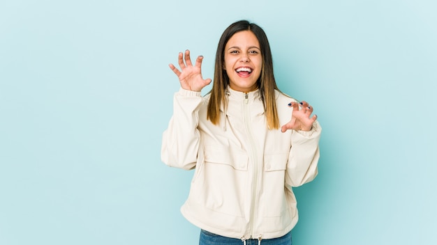 Young woman isolated on blue showing claws imitating a cat, aggressive gesture.