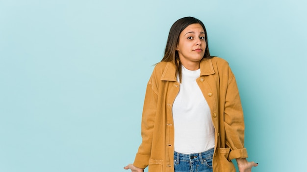 Young woman isolated on blue shrugs shoulders and open eyes confused.