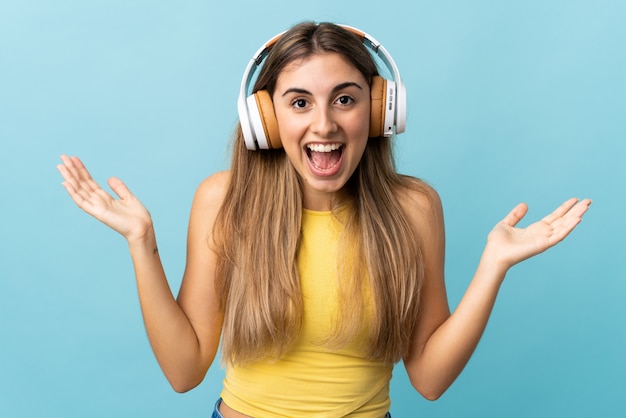 Young woman over isolated blue surprised and listening music