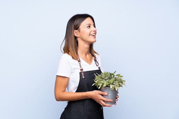 Young woman over isolated blue taking a flowerpot