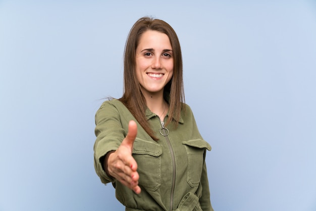 Young woman over isolated blue wall handshaking after good deal