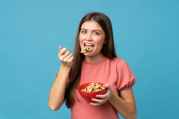 Young woman over isolated blue wall holding a bowl of cereals