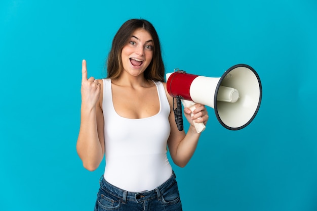 Young woman isolated on blue wall holding a megaphone and pointing up a great idea