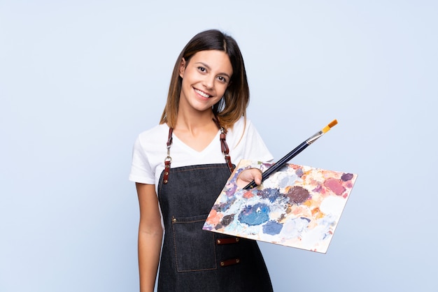 Young woman over isolated blue wall holding a palette