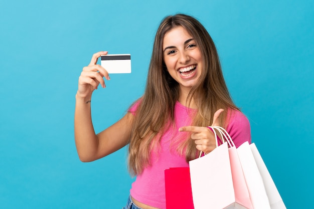 Photo young woman over isolated blue wall holding shopping bags and a credit card