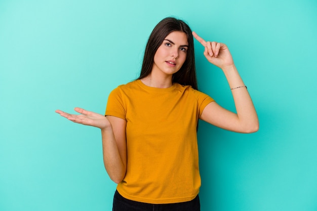 Young woman isolated on blue wall holding and showing a product on hand