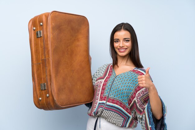 Young woman over isolated blue wall holding a vintage briefcase