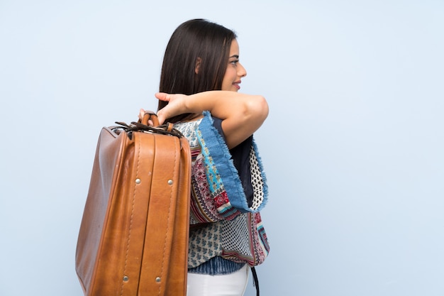 Young woman over isolated blue wall holding a vintage briefcase