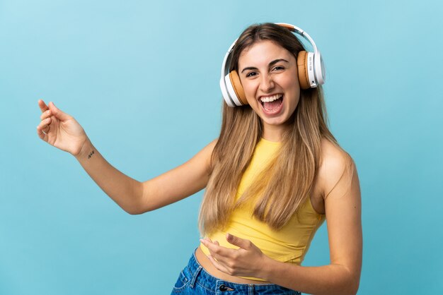 音楽を聴くとギターのジェスチャーを行う分離の青い壁の上の若い女性