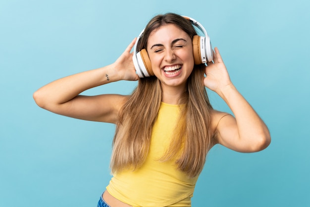 Young woman over isolated blue wall listening music