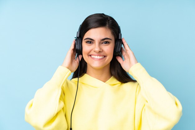 Young woman over isolated blue wall listening music