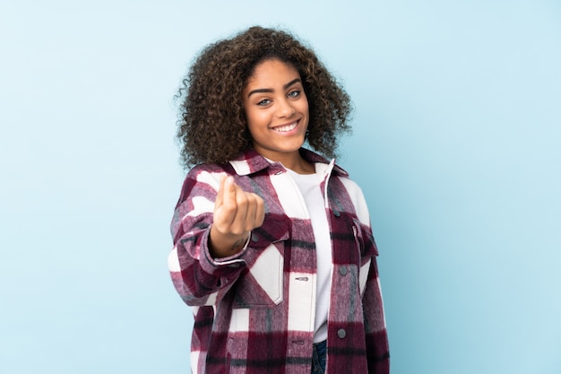 Young woman isolated on blue wall making money gesture