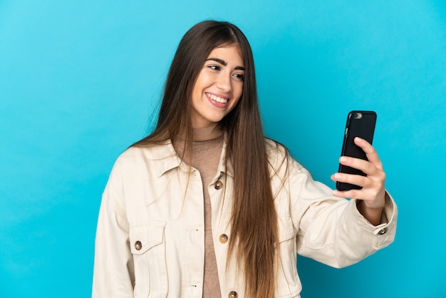 Giovane donna isolata sulla parete blu che fa un selfie